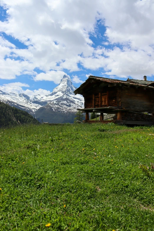 wooden cabin sitting on grassy slope with mountains in the background