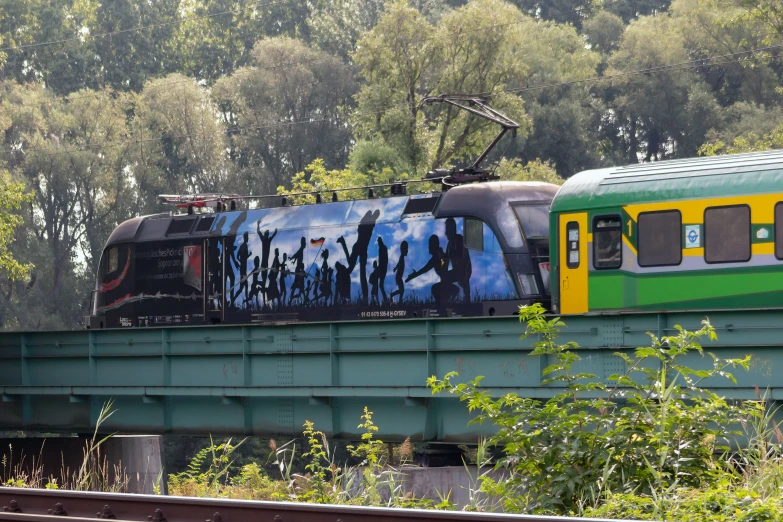 a train on the tracks on a bridge with trees in the background