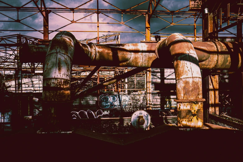 a rusty pipe near many metal structures under a cloudy sky