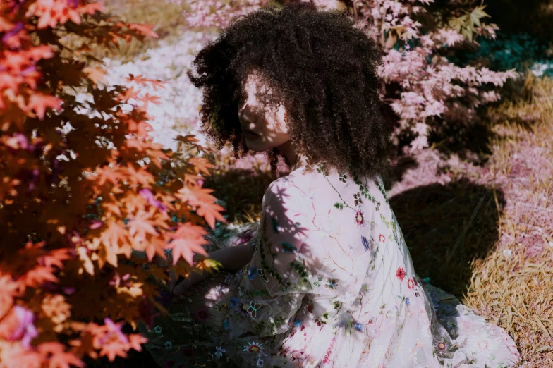 a girl with a large afro sits on the grass by flowers