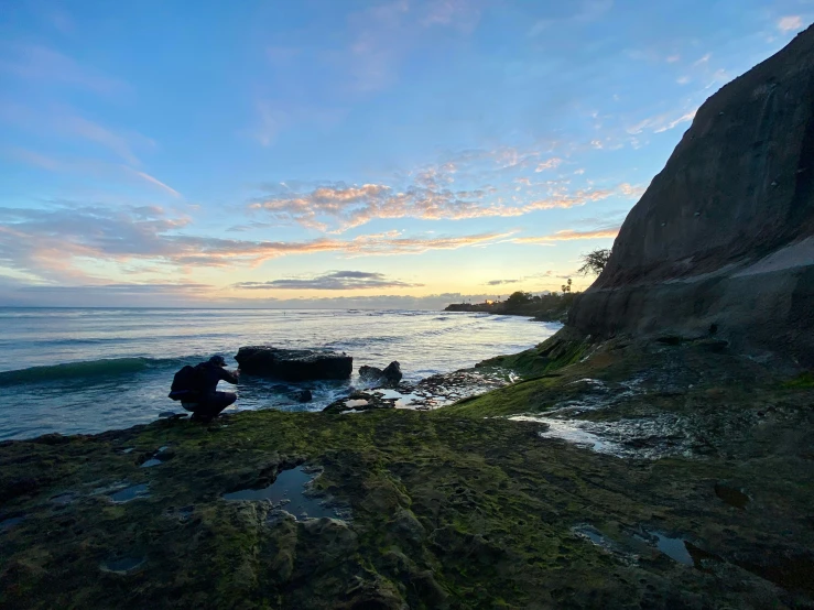 a man stands alone on a rocky cliff beside the water and trees