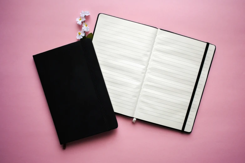 a plain black notebook next to a flower