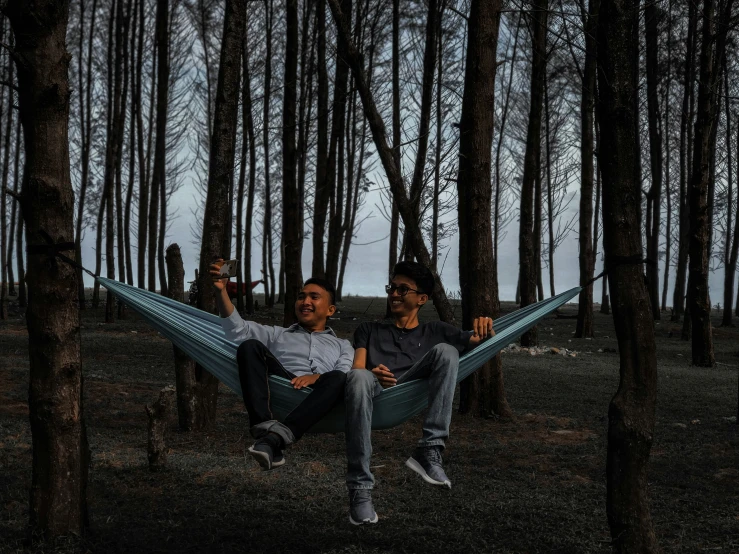 two men sit in a hammock amongst some trees