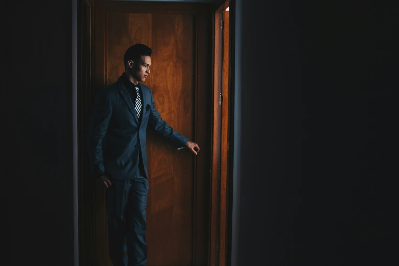 a man in a suit standing against a wooden door