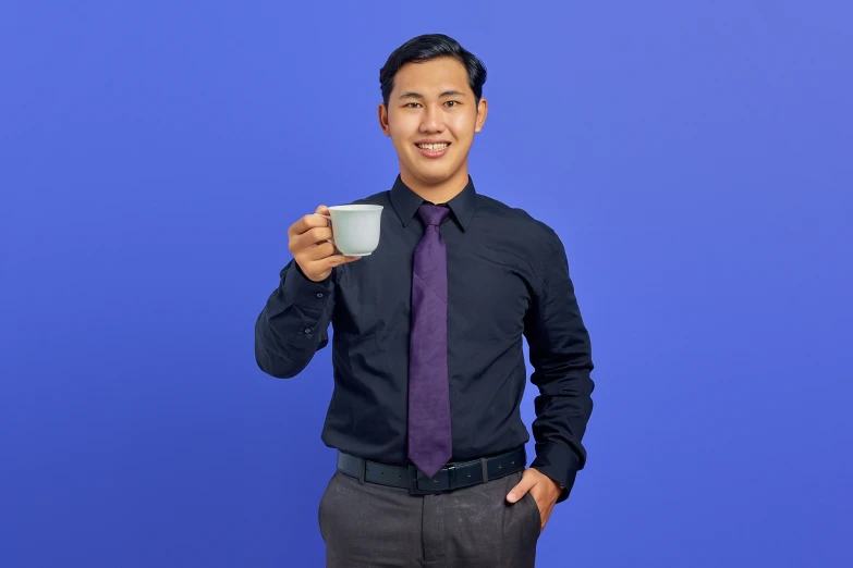a smiling young man in a business suit holds a coffee cup and points his finger