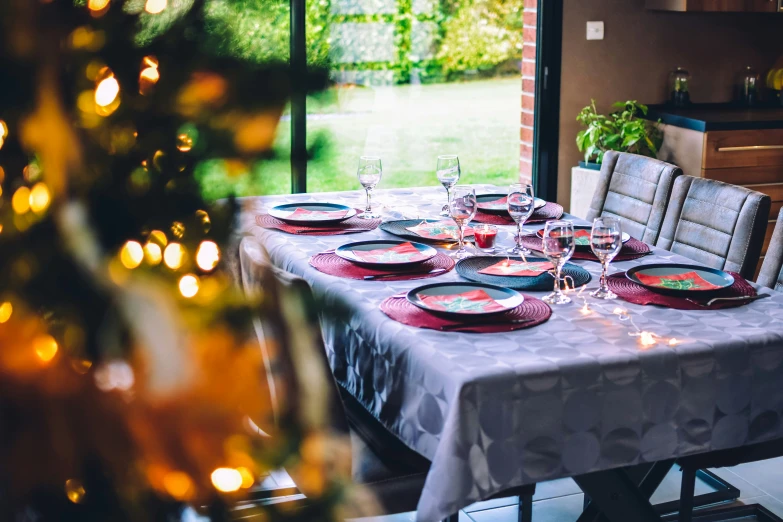 a table set with glasses, plates and candles is in the center of a dining room with many windows that look out onto an outside