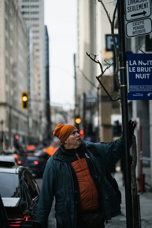 a man wearing an orange hat stands on the sidewalk next to a pole