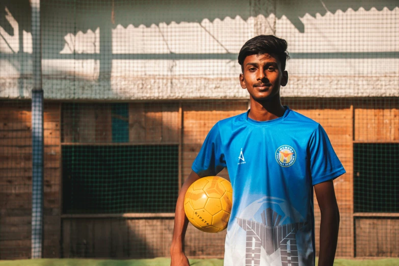 a young man holds a yellow soccer ball