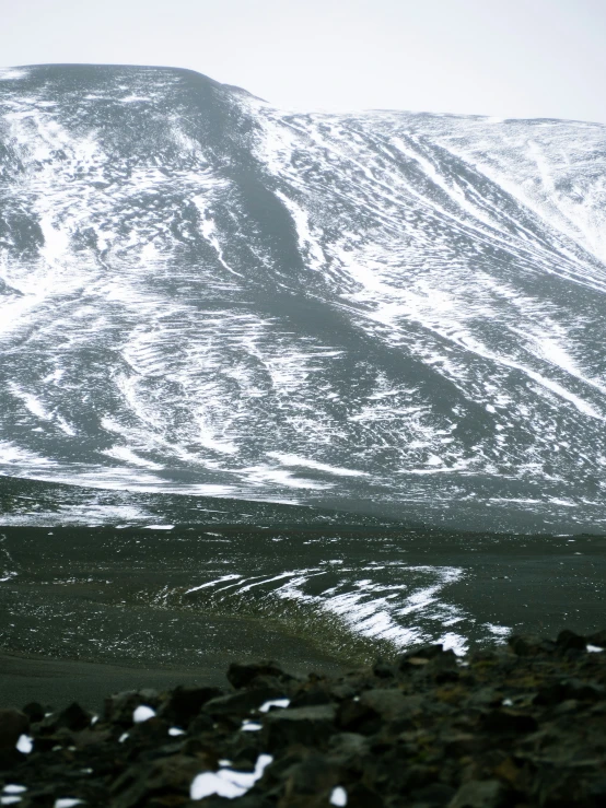 some snow rocks bushes and hills with a mountain