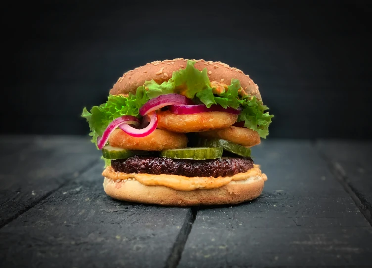 a burger with onion, lettuce and pickles on top