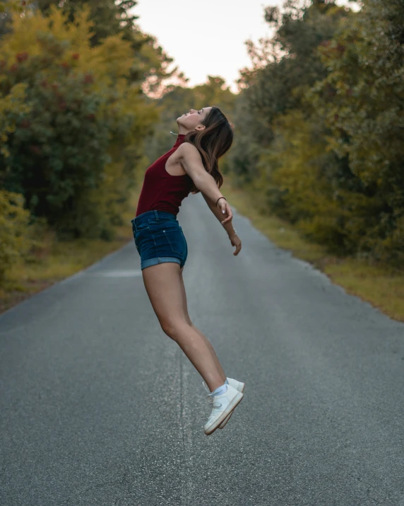 a girl jumping on a long road in a red shirt and shorts