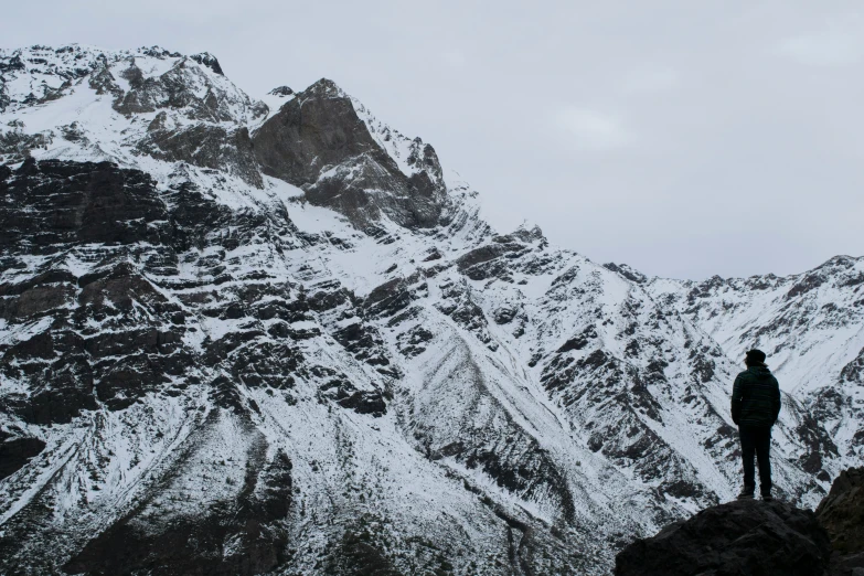 someone standing at the top of a mountain with a snow covered peak behind him