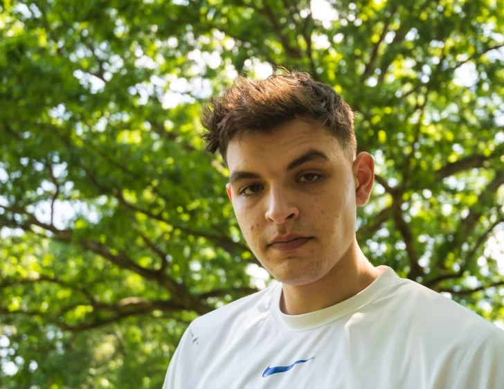 a young man stands under a tree looking at the camera