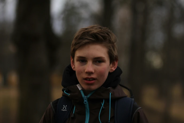 a boy wearing a jacket with hood on standing in the woods