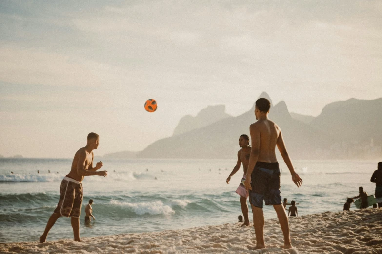 several people standing on a beach while a ball is in the air