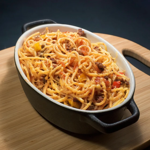 a bowl with spaghetti, meat and pepperoni sitting on a  board