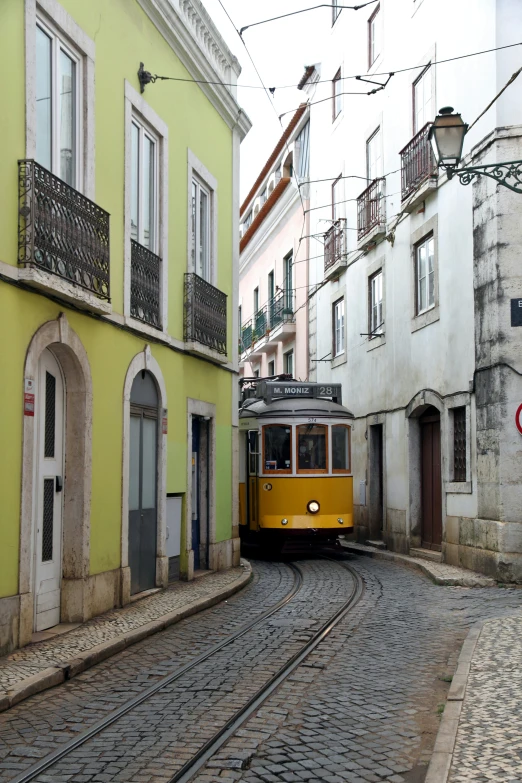 yellow train traveling through an alleyway between two buildings