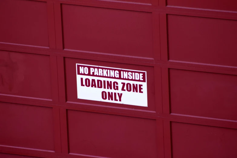 a red garage door has a no parking inside loading zone sign on it