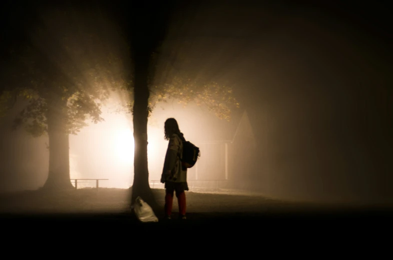 a person standing on the sidewalk at night in a foggy area