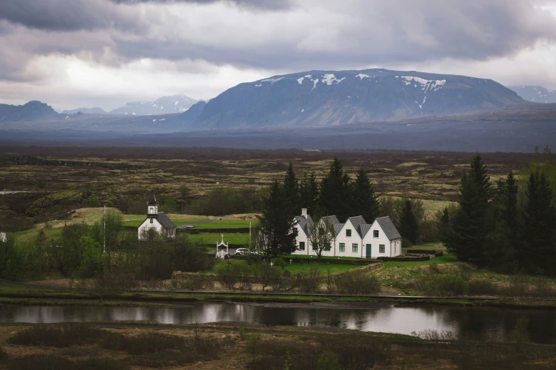 a house sitting on the side of a river near some hills