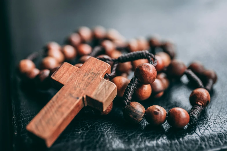 wooden rosary on black background with wood cross on it