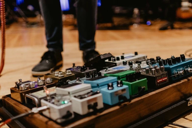 a person wearing black sneakers standing next to multiple different types of pedals on a wooden box