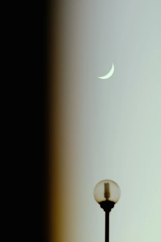 the crescent moon shines behind an old lamp post