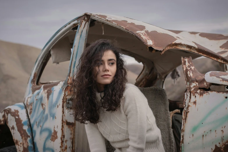 a woman leans against an old car with paint splattered all over it