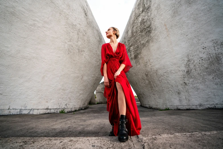 a girl wearing a red dress standing in an area with stone wall