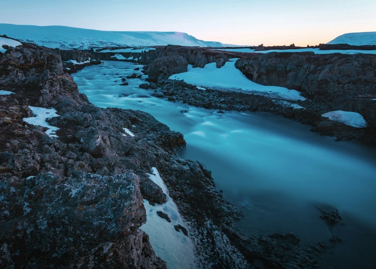 a snow - covered mountain is surrounded by water at dusk