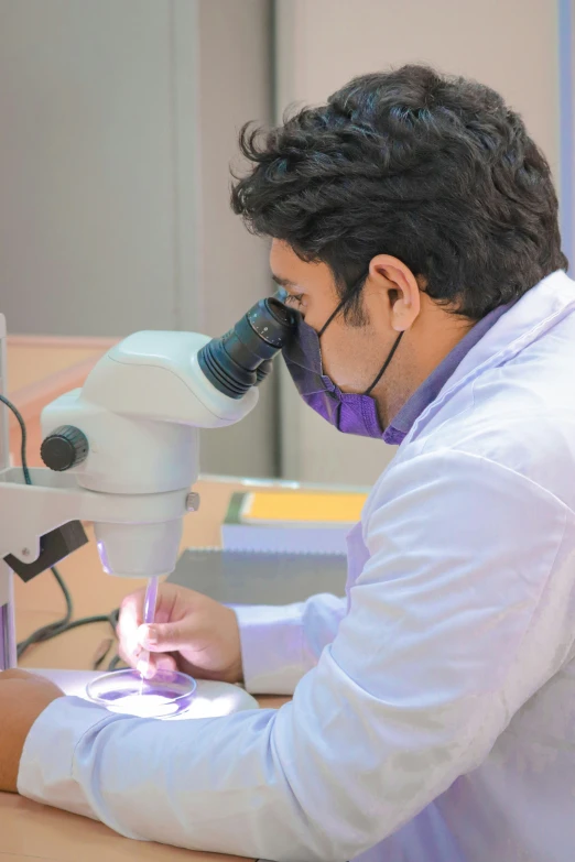 the man is wearing a hoodie and looking into a microscope