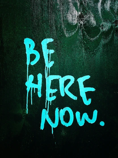 the words be here now are spray painted on the wall