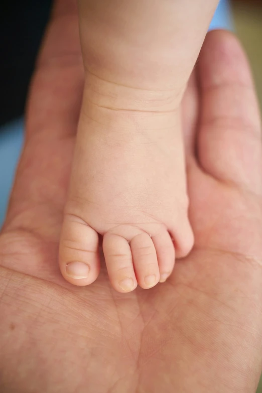baby holding the foot of an adult as they walk down a hallway
