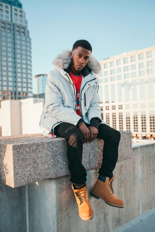 a man wearing an orange shirt and black jeans sitting on a wall