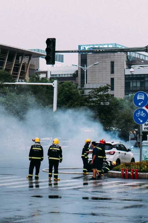 two firefighters and a car are on the road, one with its front wheels in the air