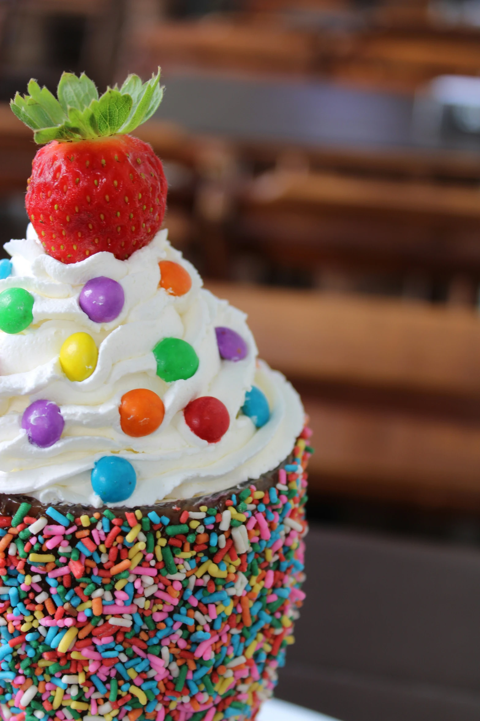 a very large colorful cupcake with white frosting and rainbow sprinkles