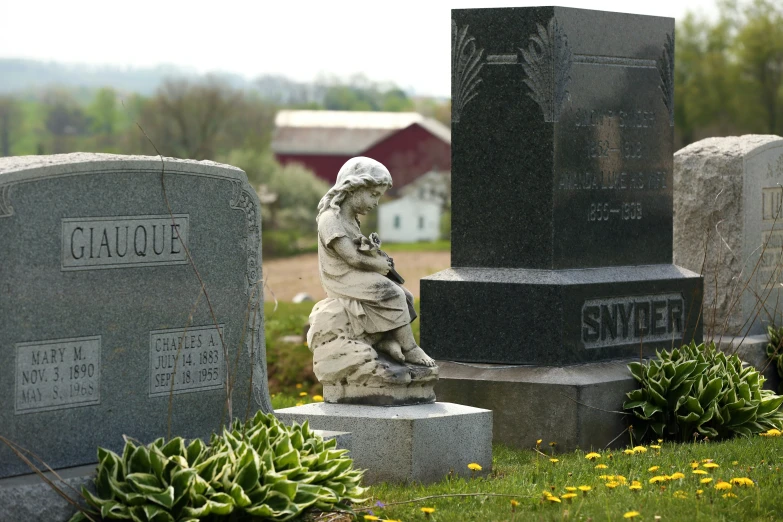 a statue sits in the grass by two headstones