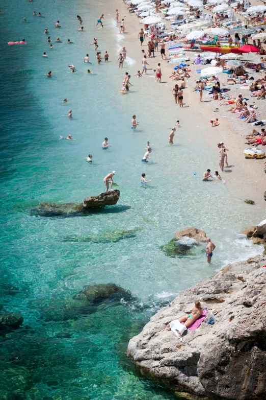 many people are on the beach near some rocks and water