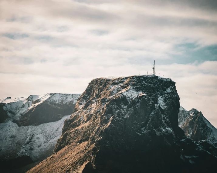 someone stands on a steep peak above the snow covered mountains