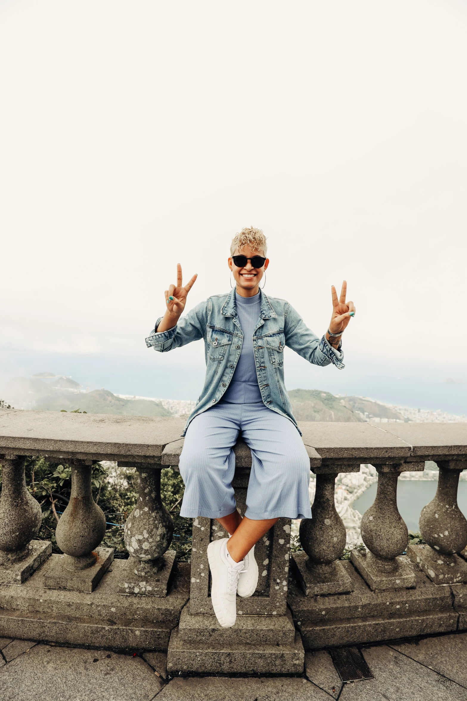 a woman sitting on a ledge while making an okay gesture