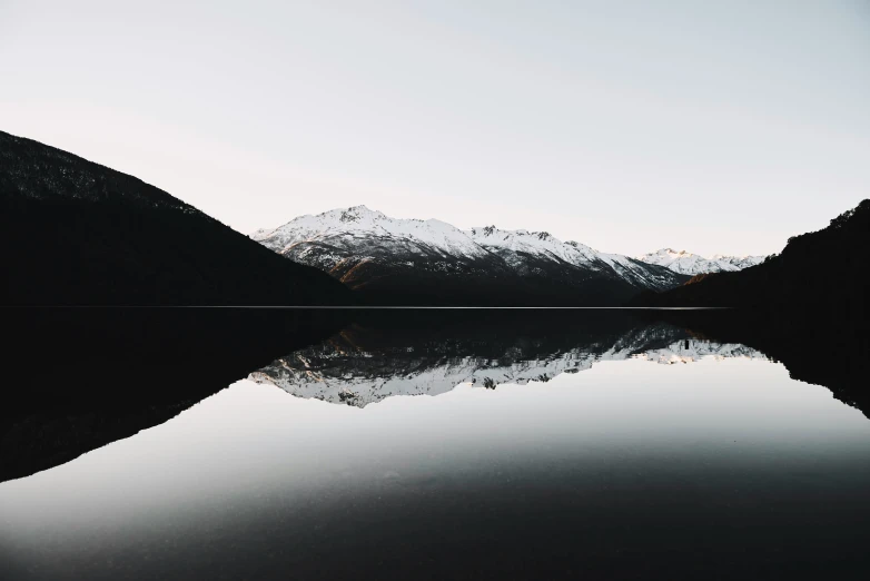a mountain range is reflected in a still body of water