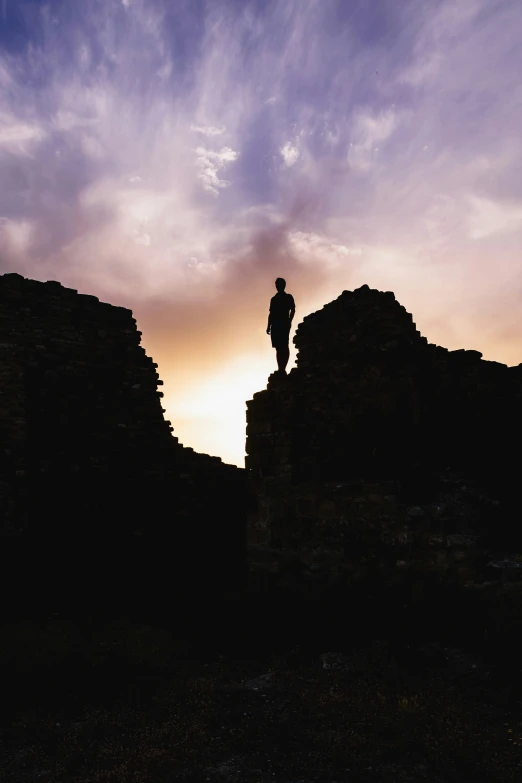 the silhouette of a person in a hat standing at the top of a rock formation