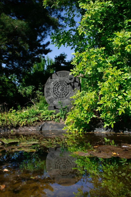 a statue sits on the bank of a pond surrounded by trees