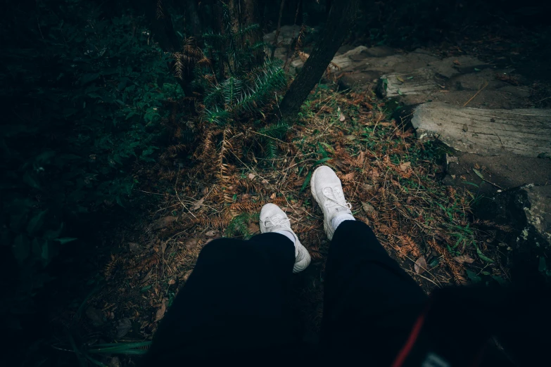 a person's feet with white shoes standing in front of a tree