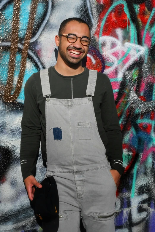 a smiling man in overalls is holding a black hat