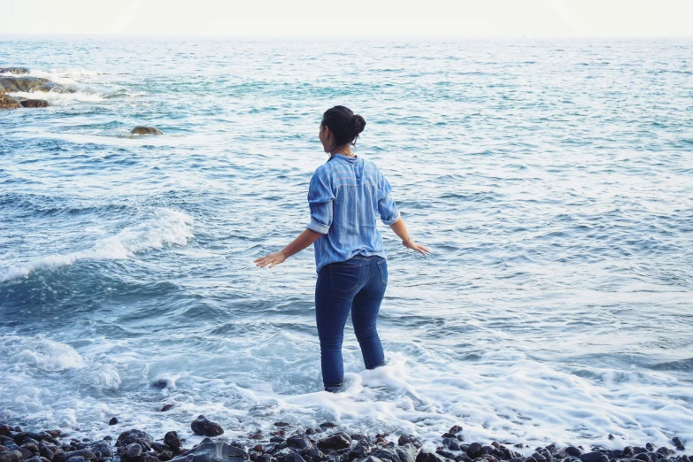 a woman standing on a rocky beach next to the ocean