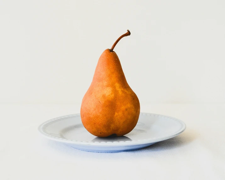 a pear sitting on a white plate against a neutral background