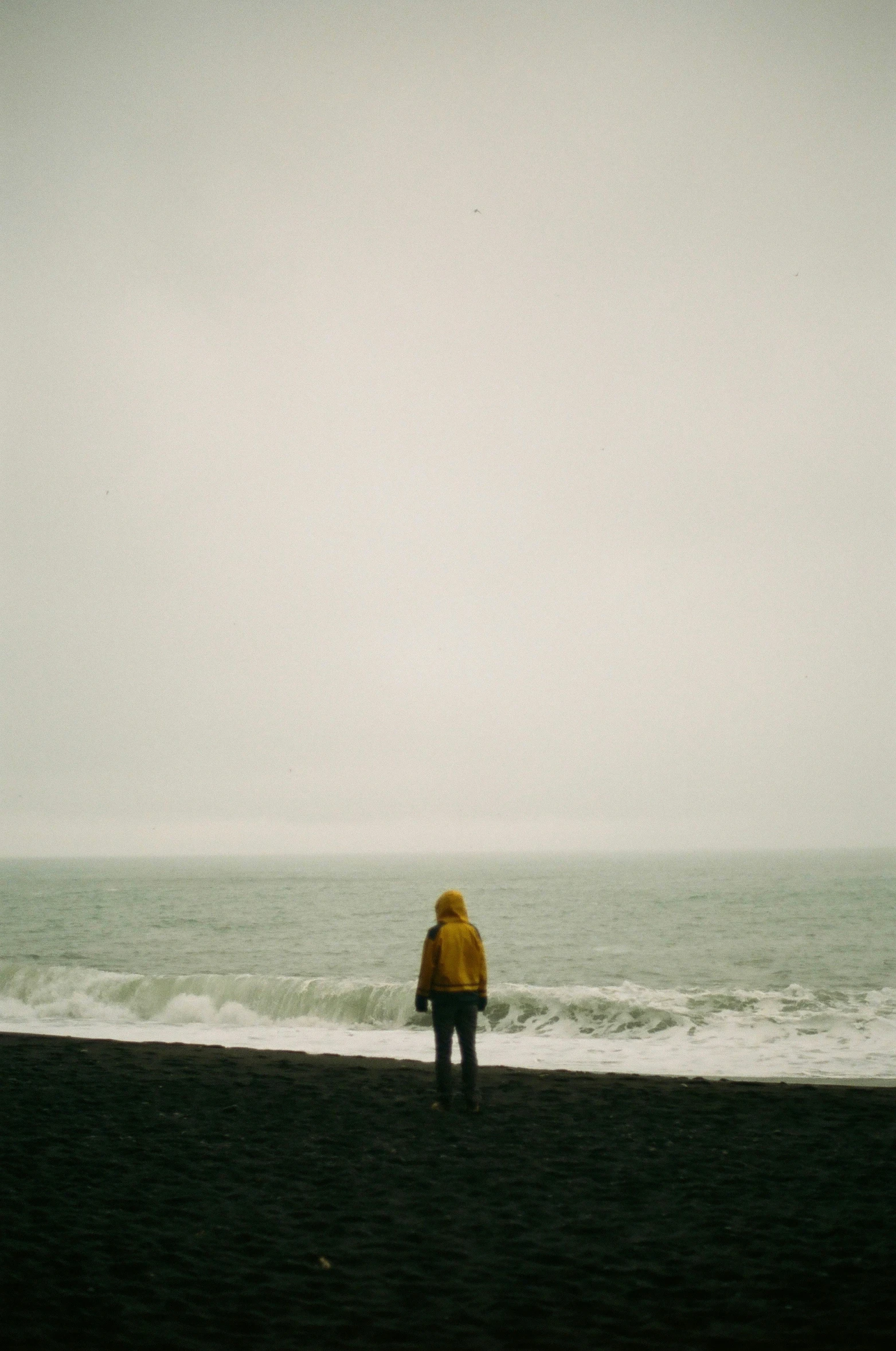 a person in a yellow jacket walking on the beach