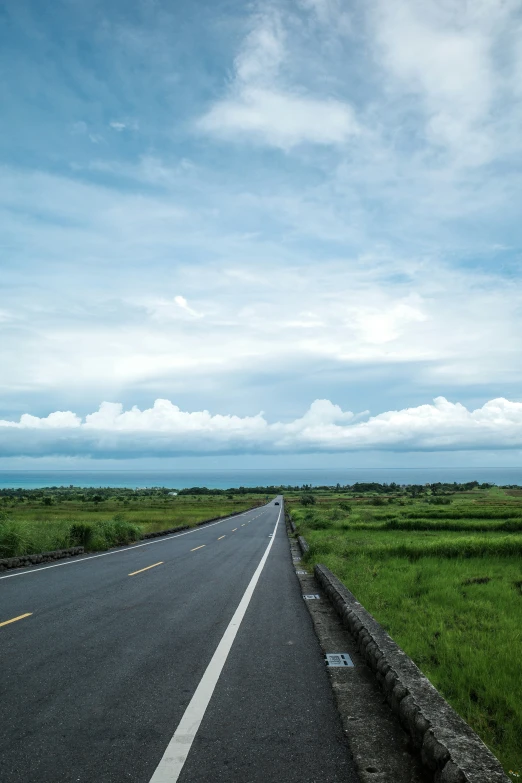 an empty road next to a field and grass