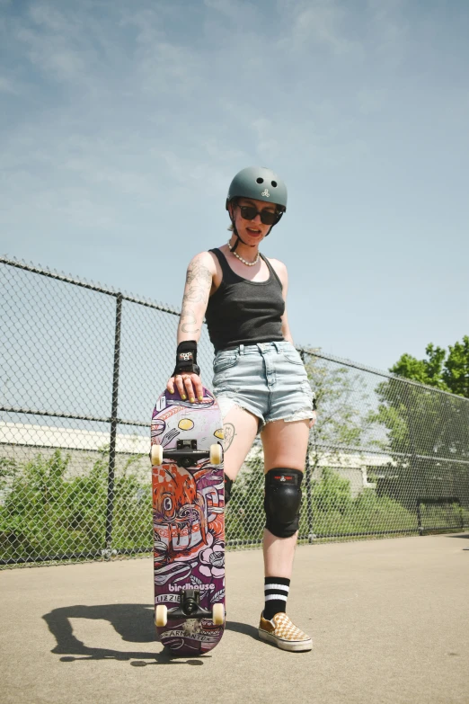 a person wearing safety pads holding a skateboard in front of a fence